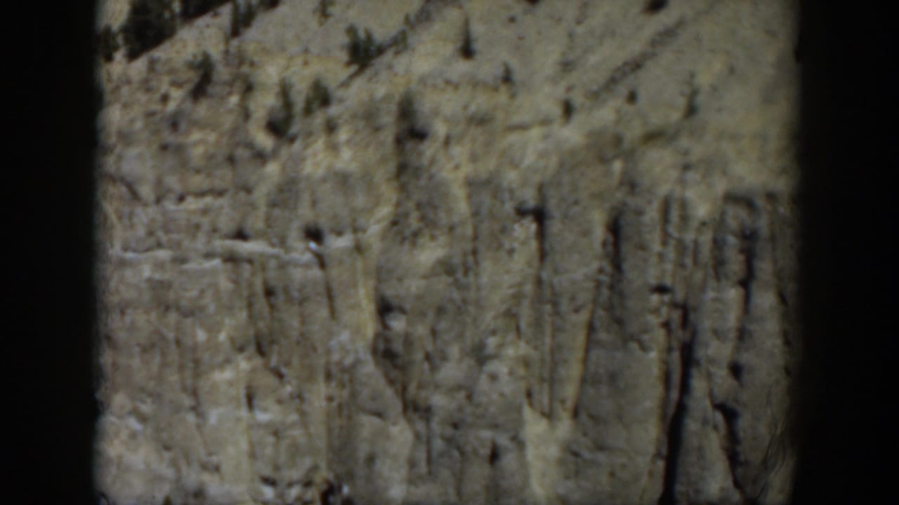 Wyoming 1951 home-movie view of an eroded rock wall with sparse trees and muted color from the 8mm source.