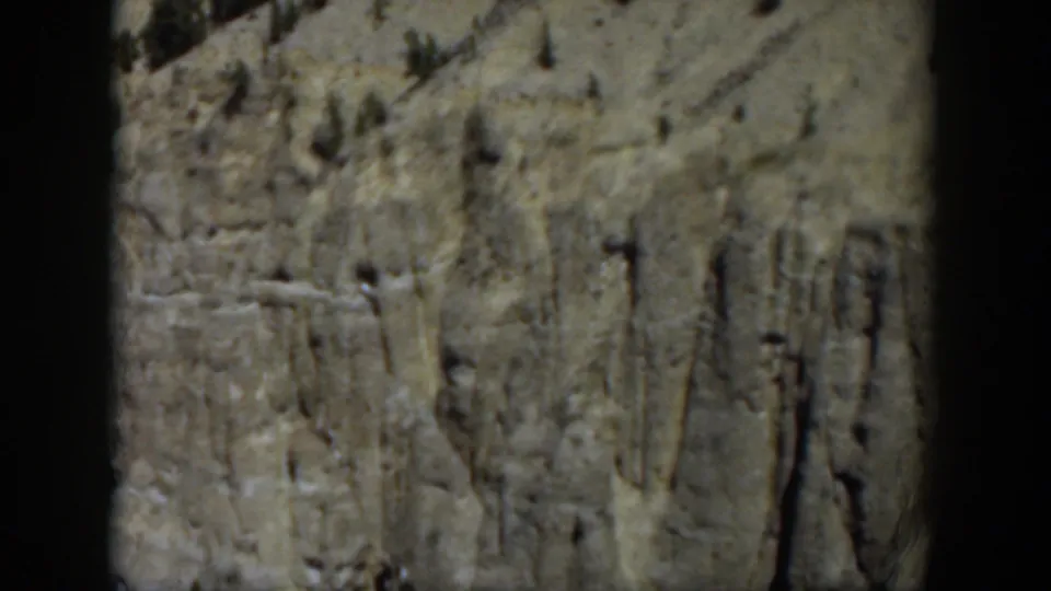 Wyoming 1951 home-movie view of an eroded rock wall with sparse trees and muted color from the 8mm source.