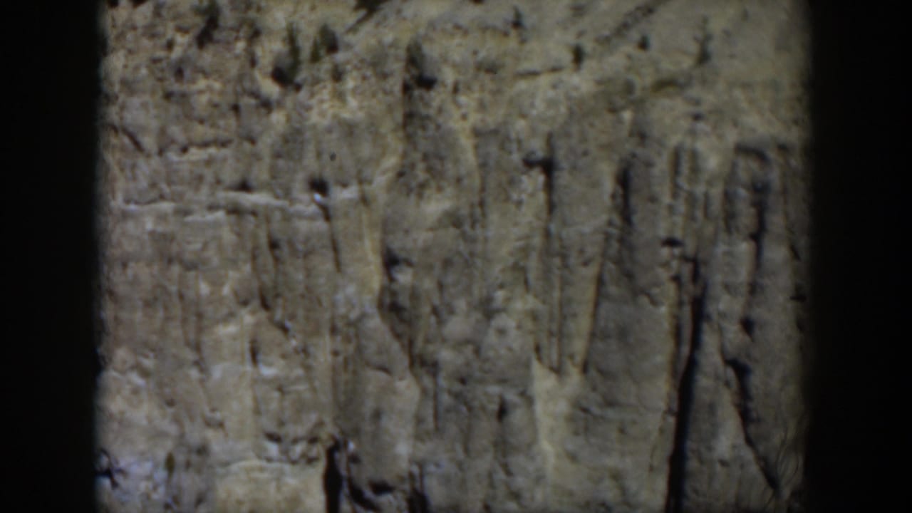 Final 1951 Wyoming frame showing a pale rock cliff, sparse pines, and dark 8mm frame edging during a handheld landscape shot.