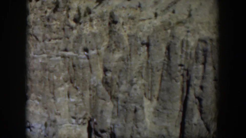 Final 1951 Wyoming frame showing a pale rock cliff, sparse pines, and dark 8mm frame edging during a handheld landscape shot.