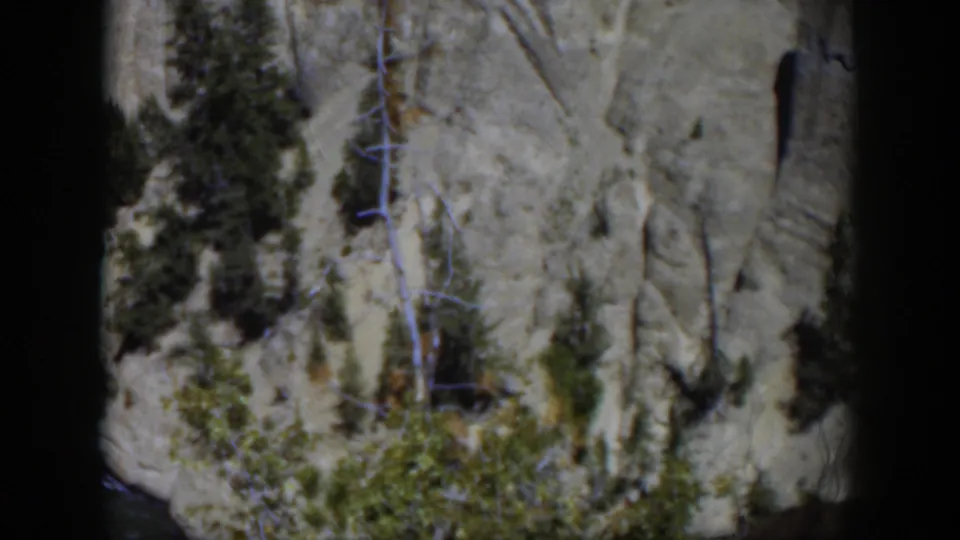 1951 Wyoming frame showing a textured gray cliff face, evergreen trees, and green brush within rounded 8mm borders.