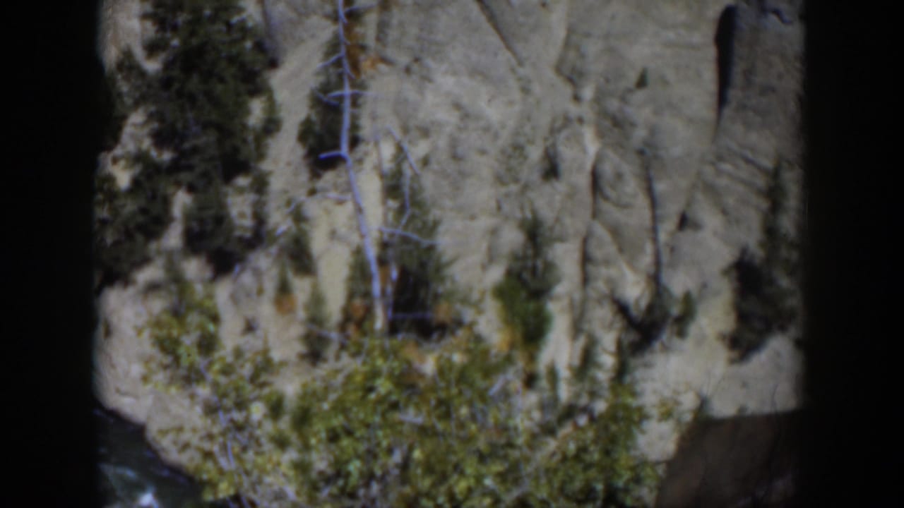 Rocky cliff face with trees and a river visible below.
