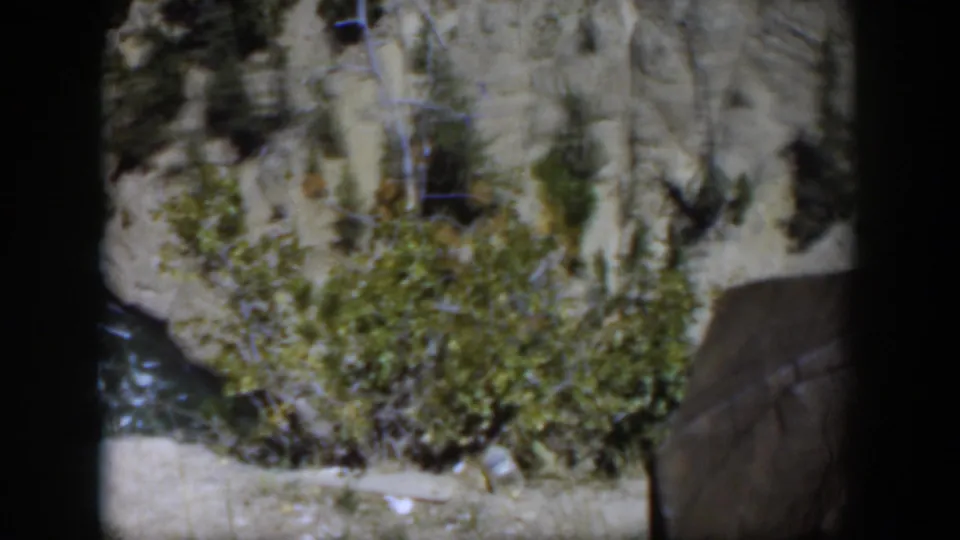 Vintage 8mm frame from Wyoming showing a downward scenic view of river water, brush, and exposed cliff stone.