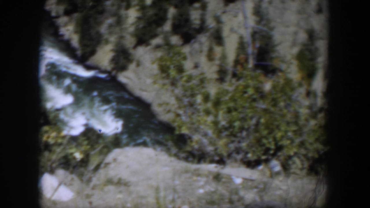 Whitewater river rushing through a rocky canyon with shrubs and black film borders.