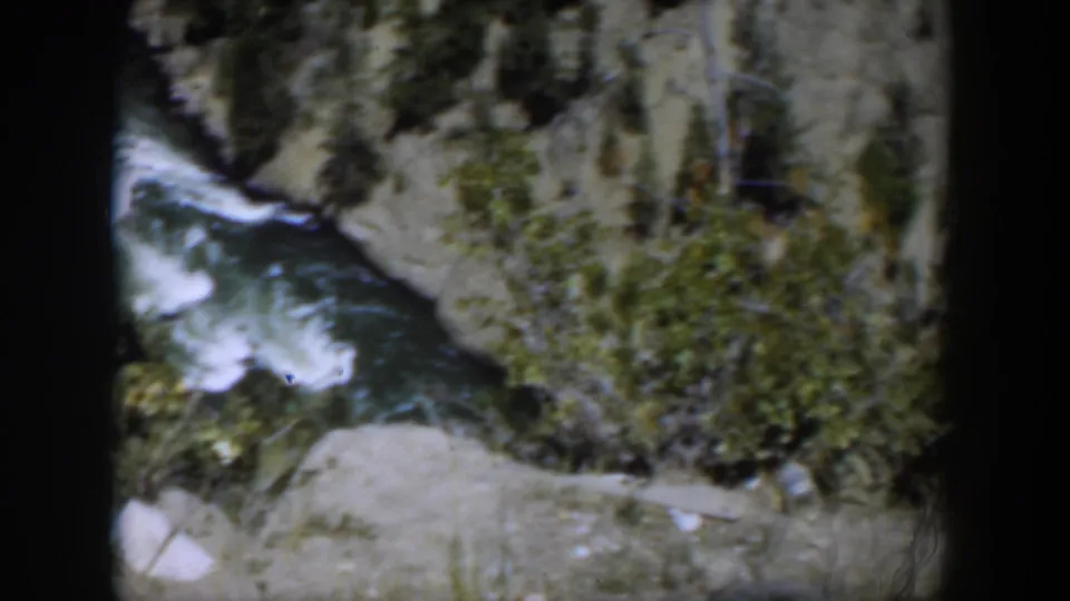 1951 Wyoming 8mm frame showing a fast river current, pale rocks, canyon banks, and sparse vegetation.