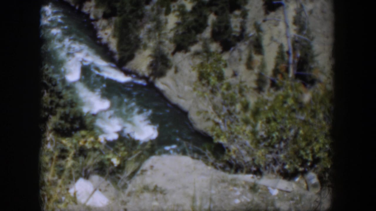 1951 Wyoming 8mm view of turbulent water bending along a rocky, brush-lined canyon channel.