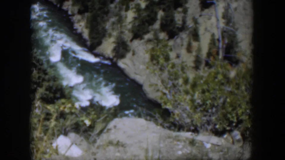 1951 Wyoming 8mm view of turbulent water bending along a rocky, brush-lined canyon channel.