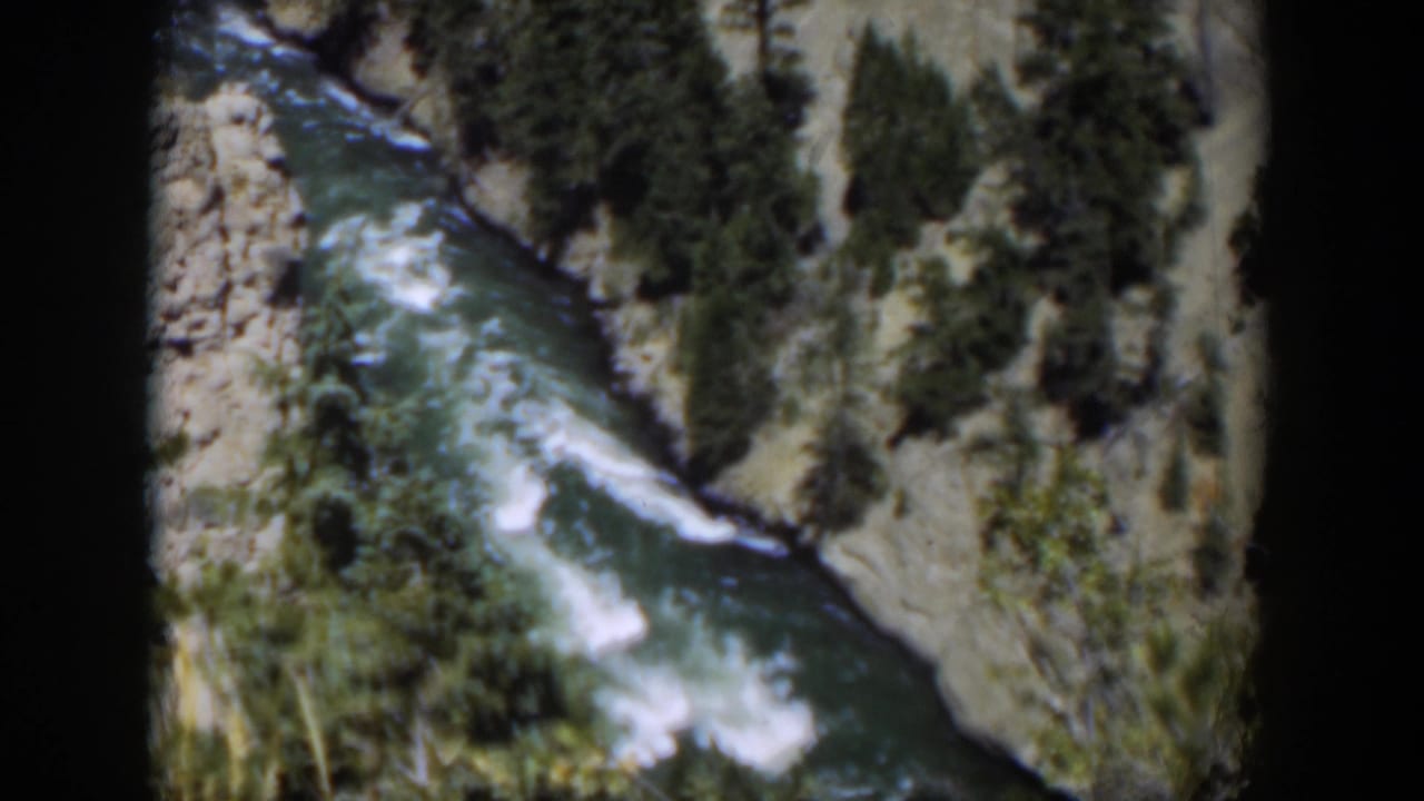1951 Wyoming 8mm frame showing whitewater moving through a narrow rocky canyon with evergreen trees on the slopes.
