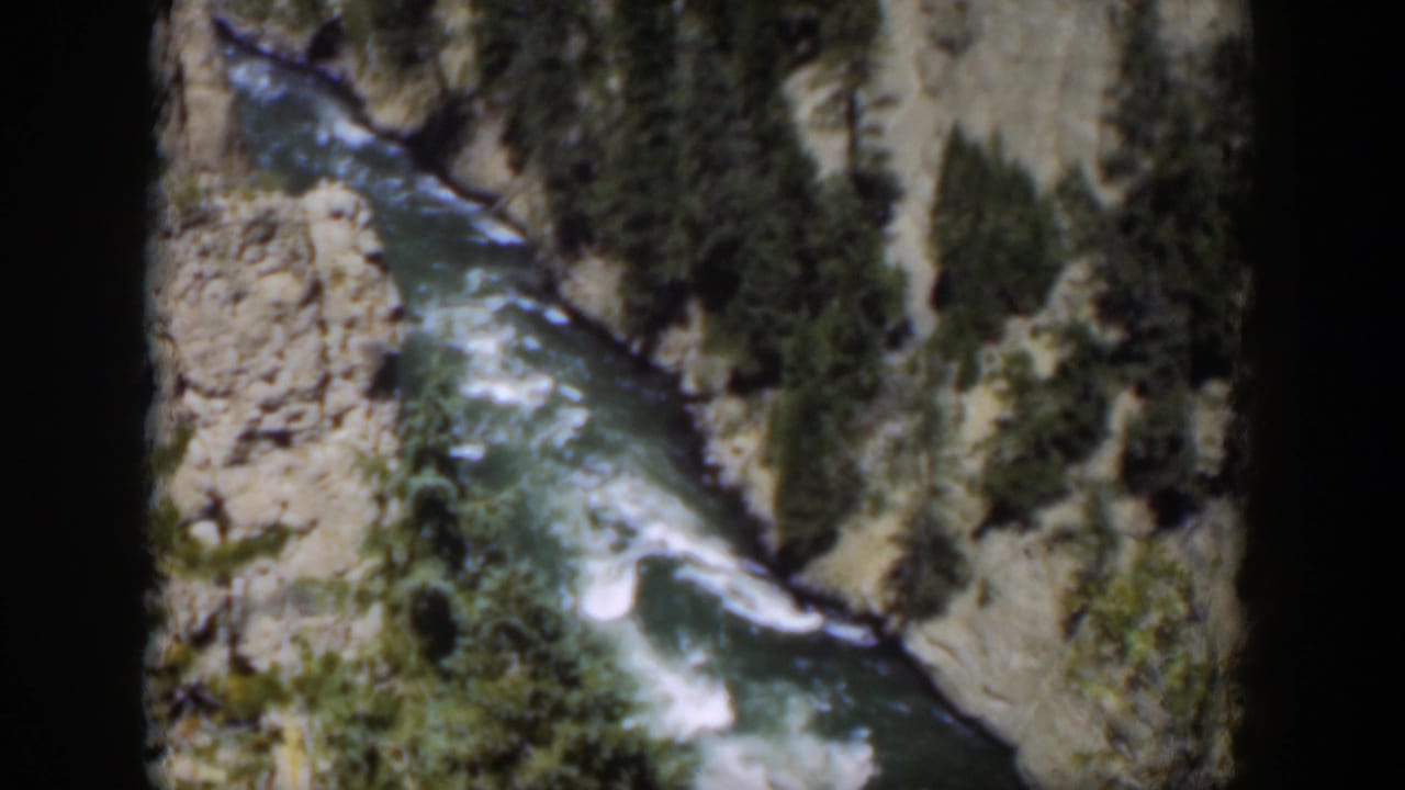 1951 Wyoming 8mm view of a fast river winding below pale canyon walls and dark conifers in bright daylight.