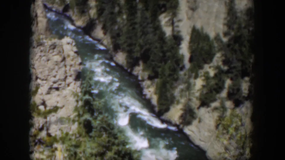 1951 Wyoming 8mm view of a fast river winding below pale canyon walls and dark conifers in bright daylight.