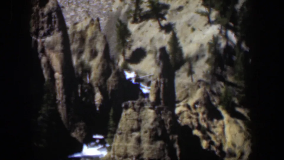 1951 8mm view of rugged Wyoming canyon rock, scattered evergreens, melting snow, and a small bright stream or waterfall below.