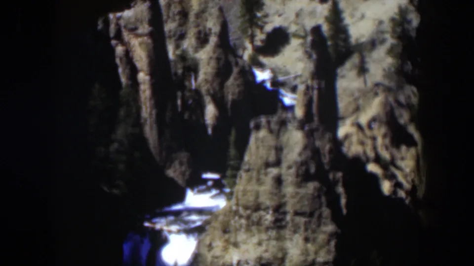 1951 Wyoming 8mm frame showing a bright waterfall between steep cracked rock faces and dark evergreens.