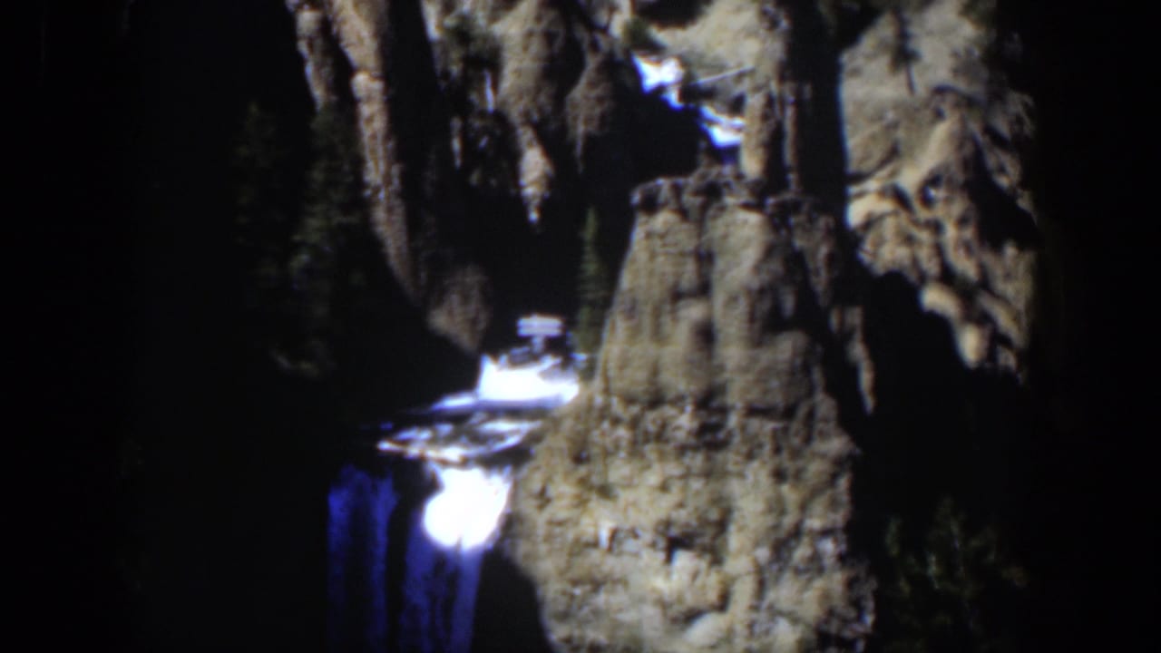 1951 Wyoming 8mm frame showing a narrow waterfall below rugged stone formations and surrounding evergreens.