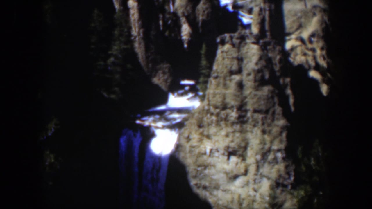 1951 Wyoming 8mm frame of a bright cascade set against cracked canyon rock and shaded evergreen forest.