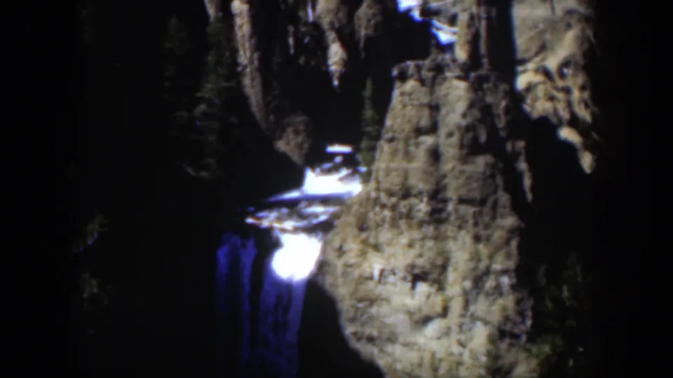 1951 Wyoming 8mm frame of a bright cascade set against cracked canyon rock and shaded evergreen forest.