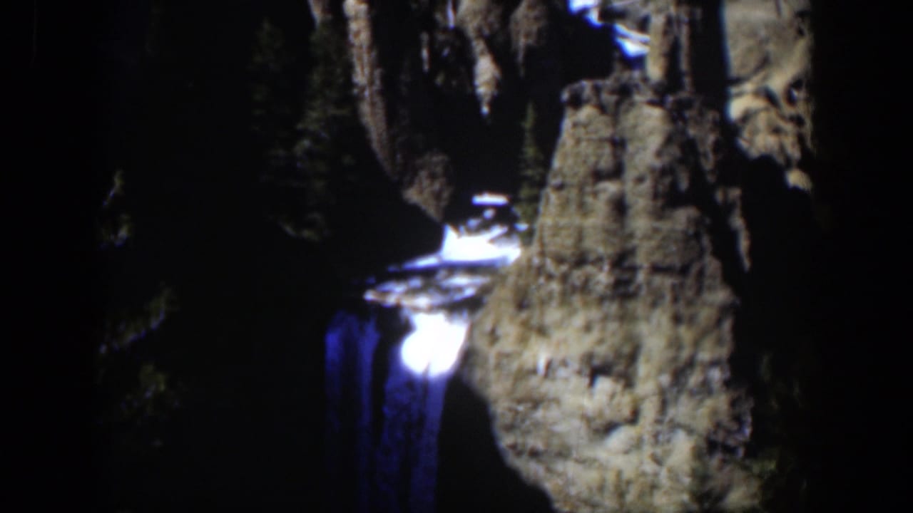 Bright waterfall lit at night beside dark rock walls and trees.
