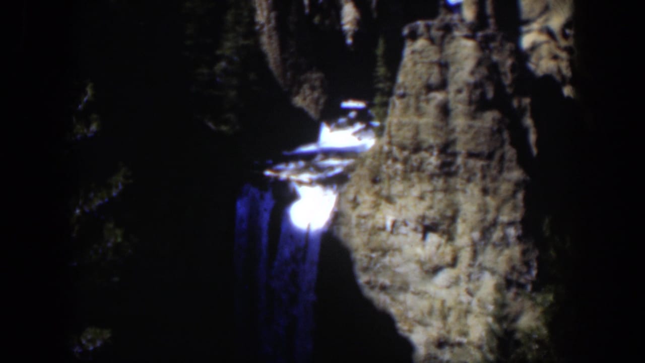 The waterfall glows white and blue beside a rough stone face in this dark 1951 Wyoming home-movie frame.