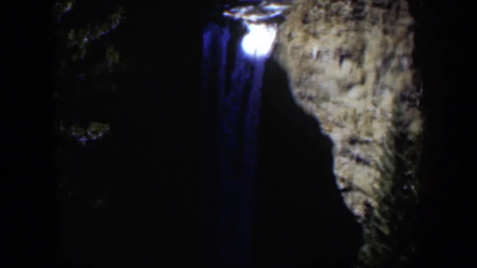 Vintage Wyoming waterfall frame with bright highlights near the top and blue falling water against a shadowed rock wall.