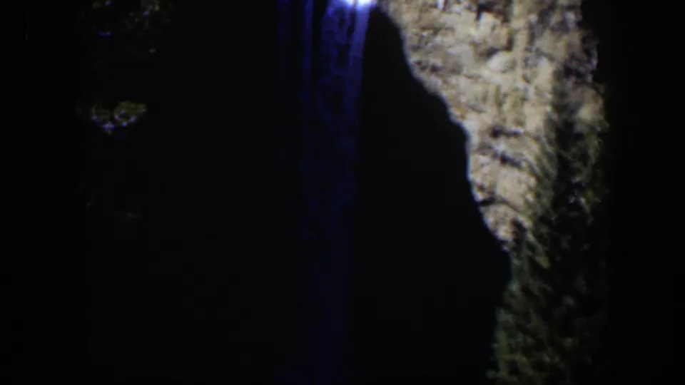 1951 8mm view of the waterfall running down a dark channel next to a close, textured cliff face.