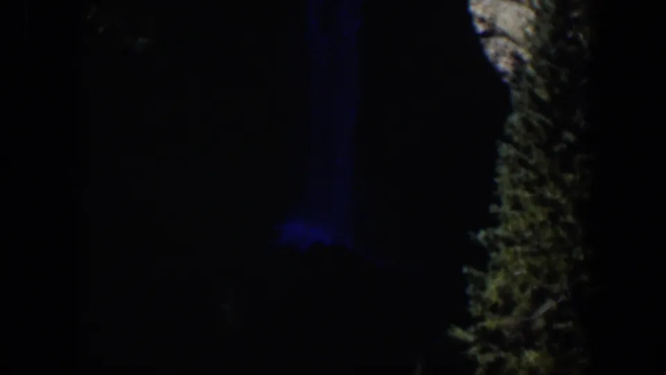 1951 Wyoming 8mm frame showing a dim outdoor scene with blue illumination and a rough vertical natural surface at the right.