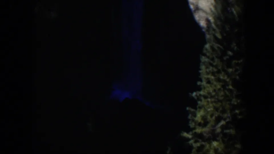Dim 1951 Wyoming home-movie frame with a blue-lit patch and a rough bark-like or rock-like vertical edge.