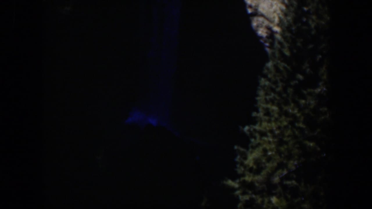 1951 Wyoming 8mm frame showing a nearly black outdoor view, blue illumination, and a rough vertical natural surface.