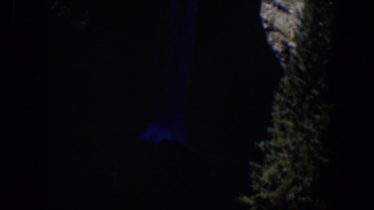Late-frame 1951 Wyoming 8mm view of a dim outdoor landscape detail with blue light and rough illuminated texture.