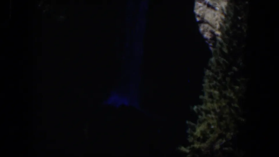 Late-frame 1951 Wyoming 8mm view of a dim outdoor landscape detail with blue light and rough illuminated texture.