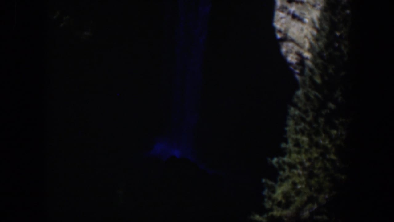 1951 Wyoming 8mm frame showing a nighttime waterfall area, blue-lit water, and a pale rocky cliff edge surrounded by darkness.