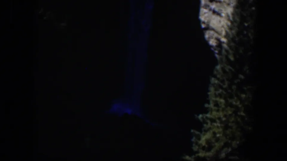 1951 Wyoming 8mm frame showing a nighttime waterfall area, blue-lit water, and a pale rocky cliff edge surrounded by darkness.
