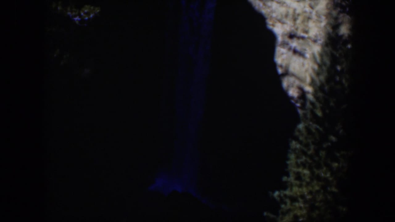 1951 Wyoming 8mm frame with a narrow blue waterfall glow and textured rock face visible against near-black surroundings.