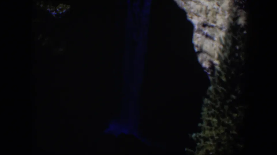 1951 Wyoming 8mm frame with a narrow blue waterfall glow and textured rock face visible against near-black surroundings.