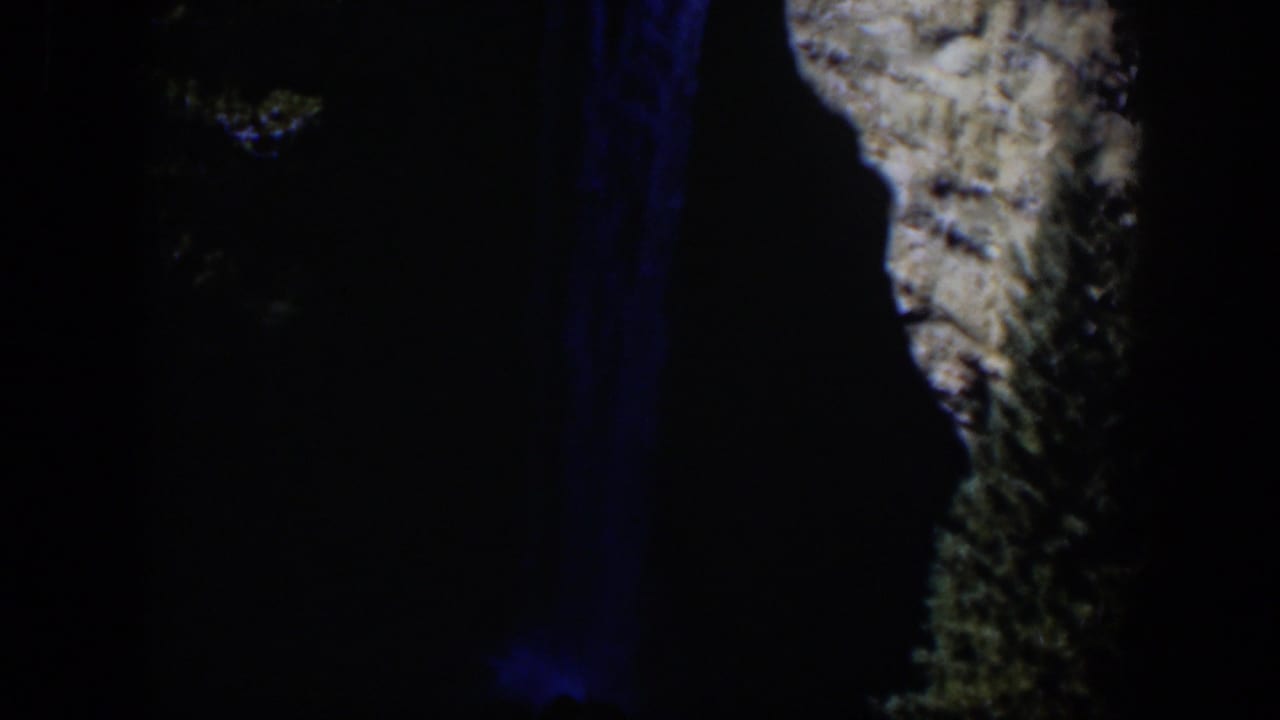 1951 Wyoming 8mm frame showing the waterfall’s blue-lit vertical streaks beside a pale, textured cliff in deep night exposure.