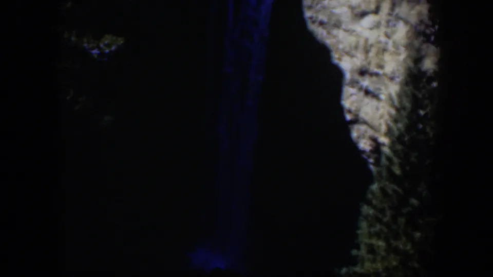 1951 Wyoming 8mm frame showing the waterfall’s blue-lit vertical streaks beside a pale, textured cliff in deep night exposure.