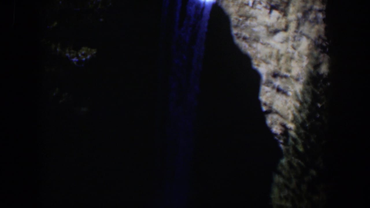1951 Wyoming 8mm frame with blue light on falling water and a pale rock wall, mostly surrounded by dark nighttime shadow.