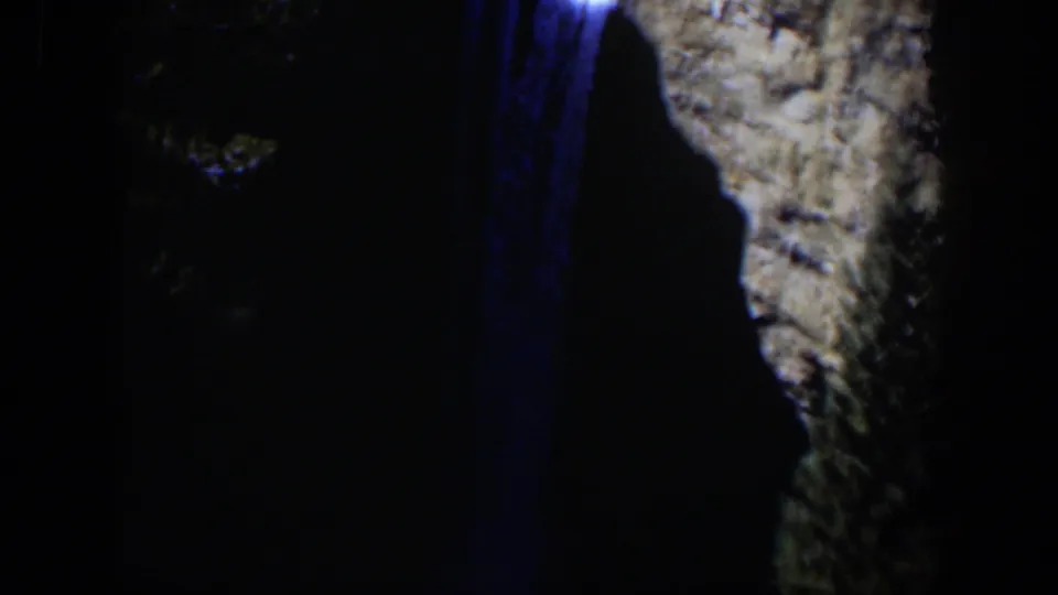 1951 Wyoming 8mm frame with blue light on falling water and a pale rock wall, mostly surrounded by dark nighttime shadow.