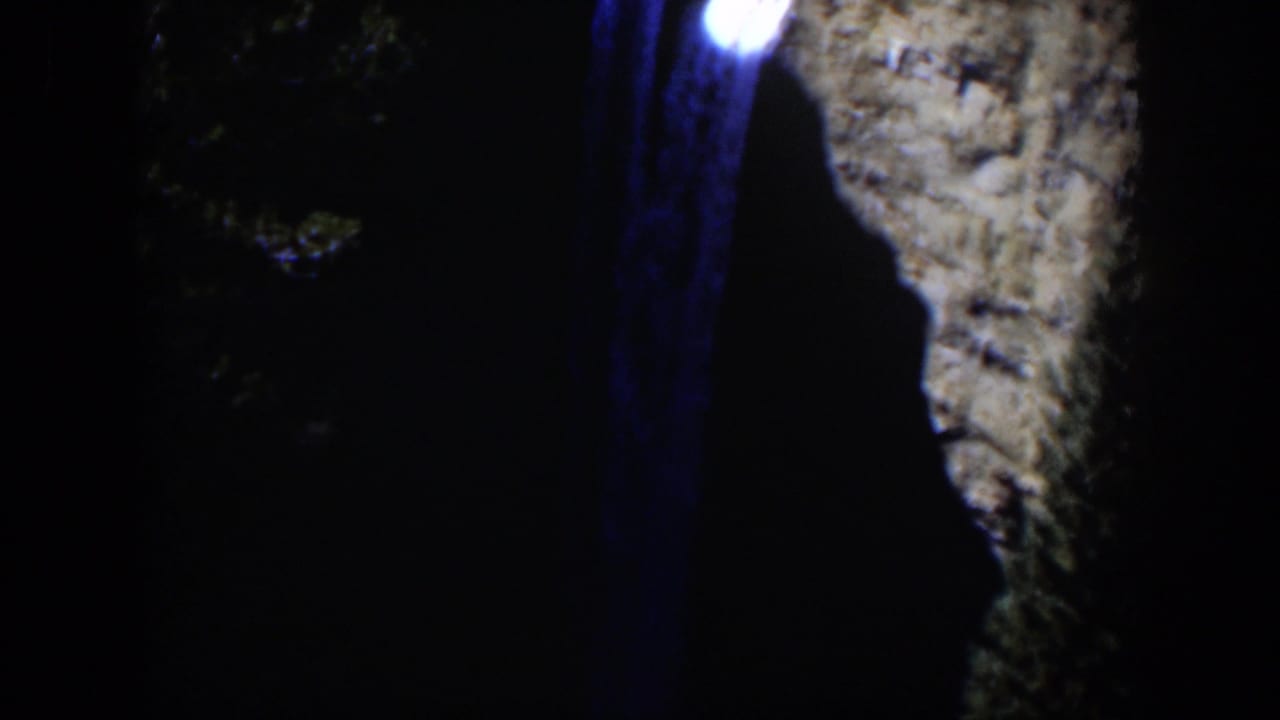 1951 Wyoming 8mm frame showing a bright light with a blue vertical streak near a shadowed canyon wall and trees.