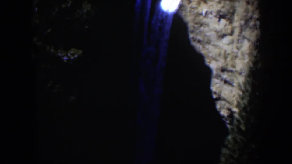 1951 Wyoming 8mm frame showing a bright light with a blue vertical streak near a shadowed canyon wall and trees.
