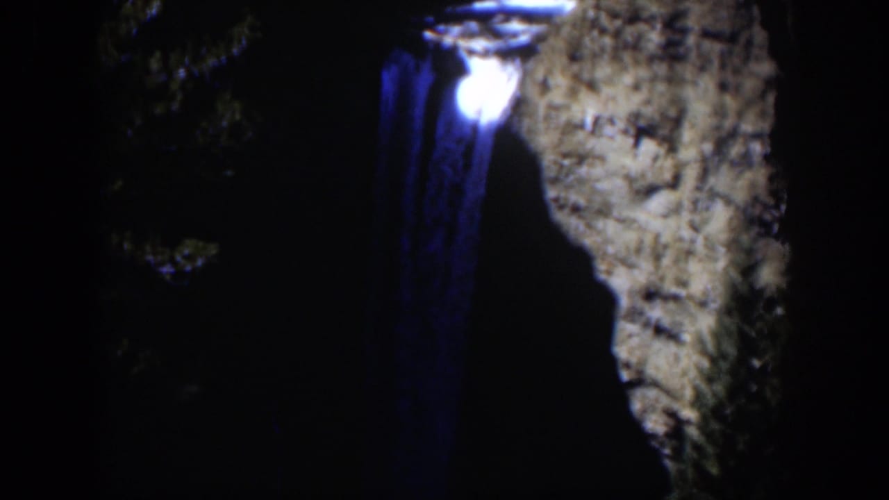 1951 Wyoming 8mm frame showing a bright light near a blue trail, framed by dark trees and a textured rock face.