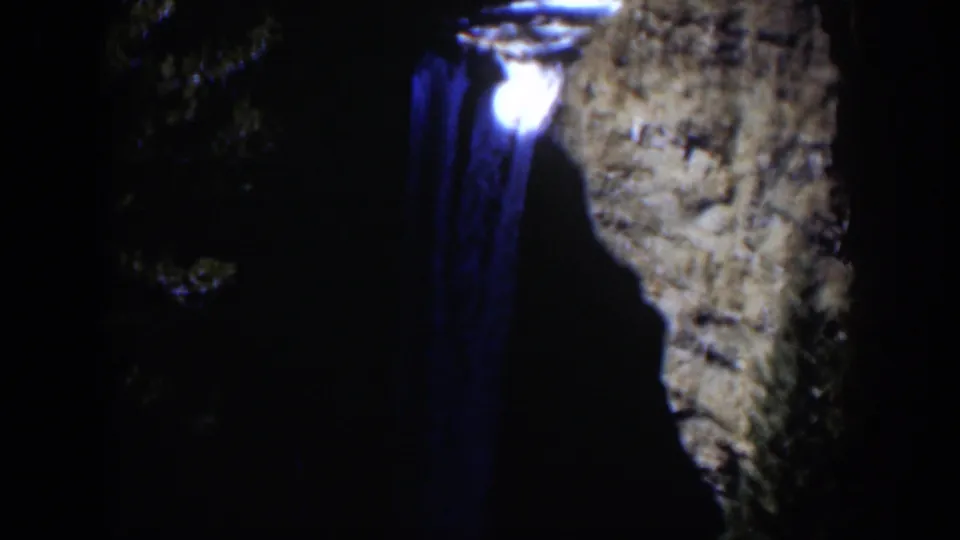 1951 Wyoming 8mm frame showing a bright light near a blue trail, framed by dark trees and a textured rock face.