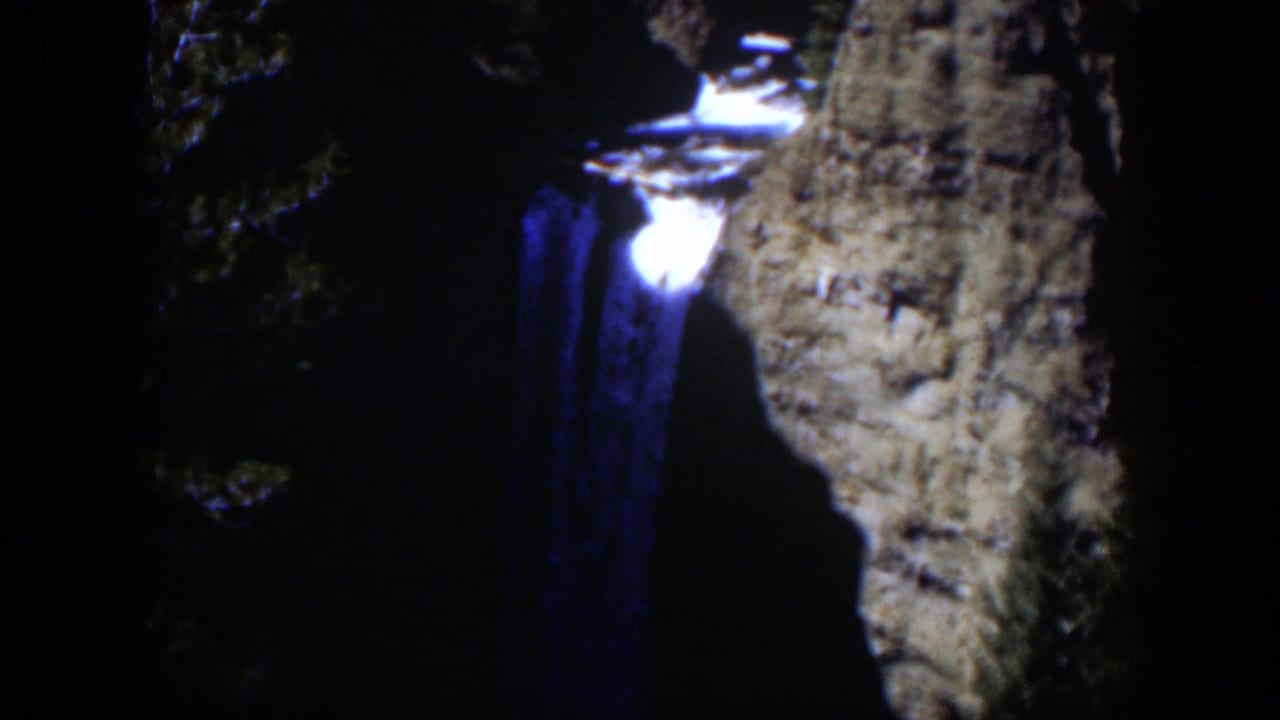 A nighttime 8mm view of the Wyoming waterfall with blue water glow, bright spill at the top, and rock wall partly lit.