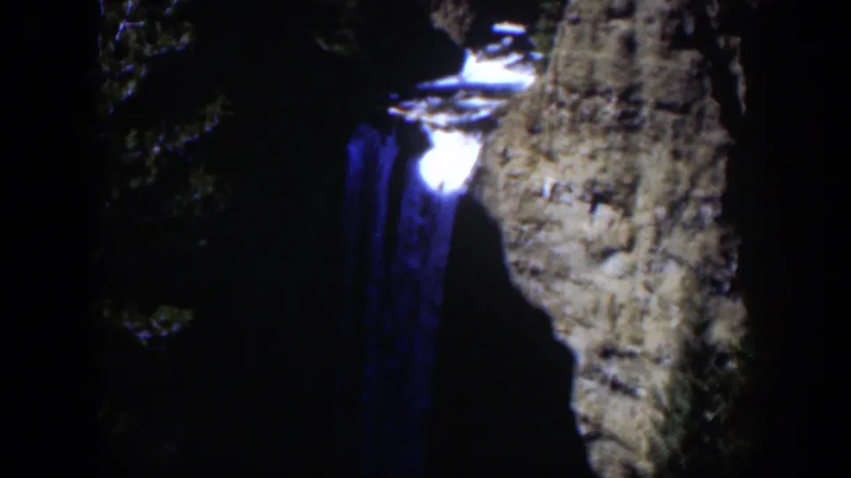 A nighttime 8mm view of the Wyoming waterfall with blue water glow, bright spill at the top, and rock wall partly lit.