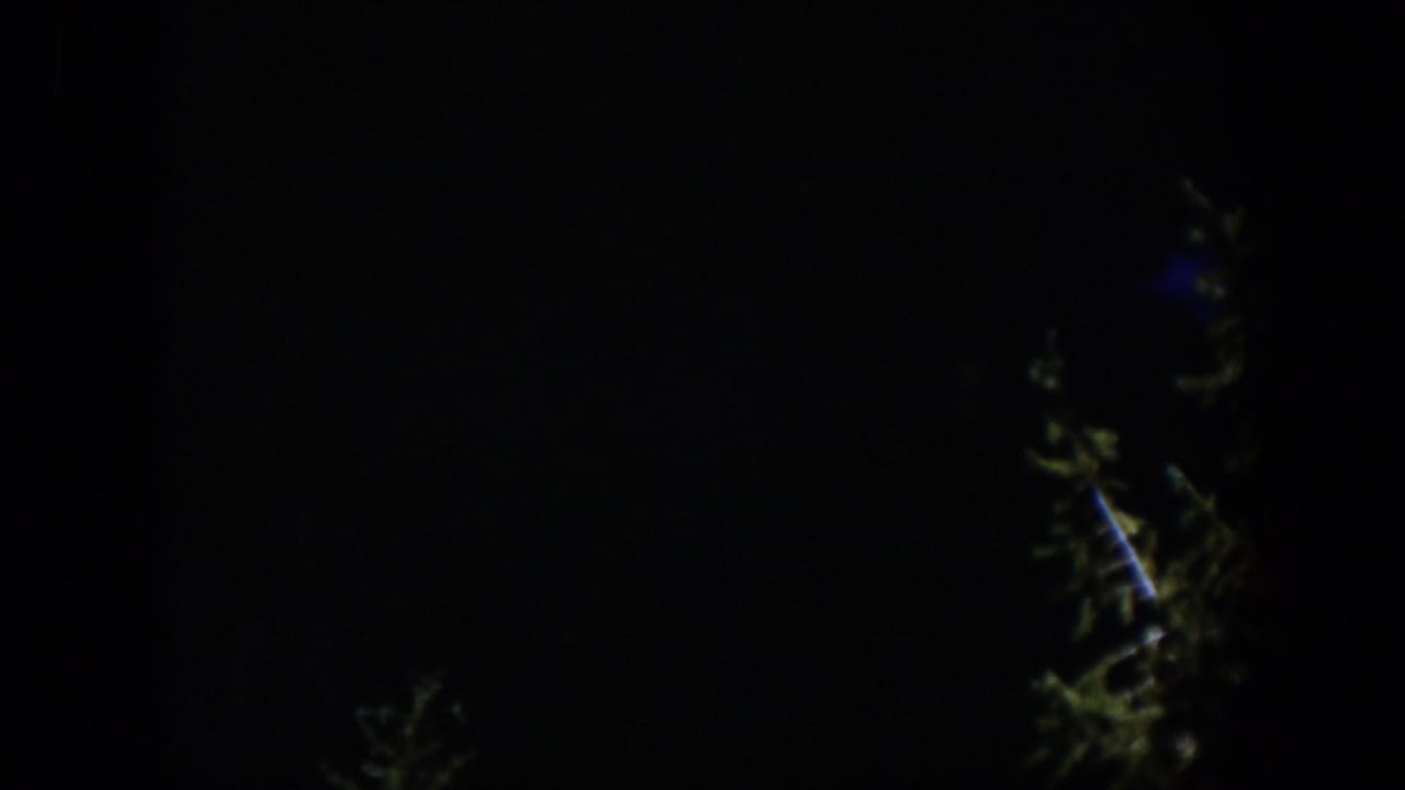 A very dark 1951 Wyoming 8mm frame where only part of the blue illuminated waterfall and nearby tree shapes remain visible.
