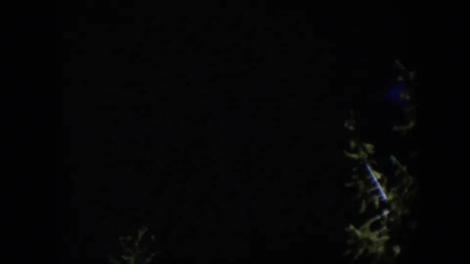 A very dark 1951 Wyoming 8mm frame where only part of the blue illuminated waterfall and nearby tree shapes remain visible.
