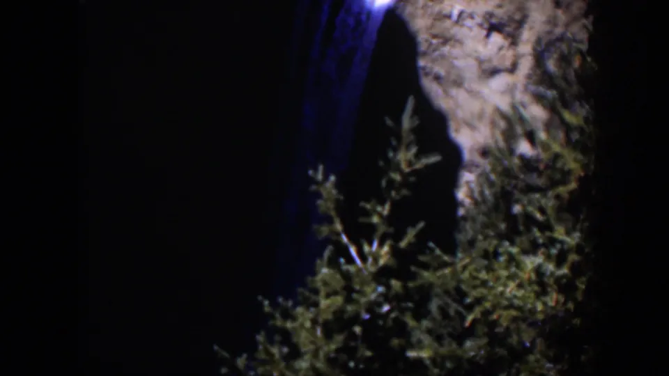 A soft 8mm view of a nighttime Wyoming waterfall framed by cliff rock and dark green foliage.