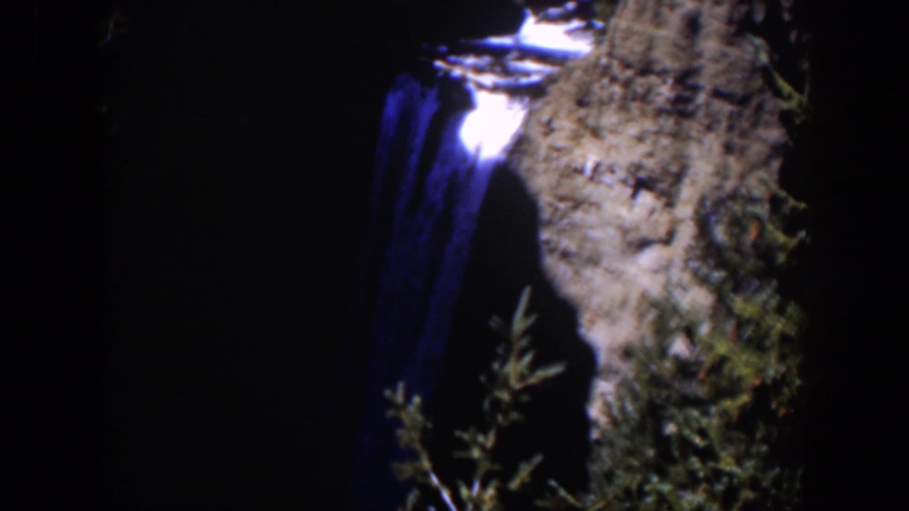 Waterfall descending beside a gray cliff in deep shadow.