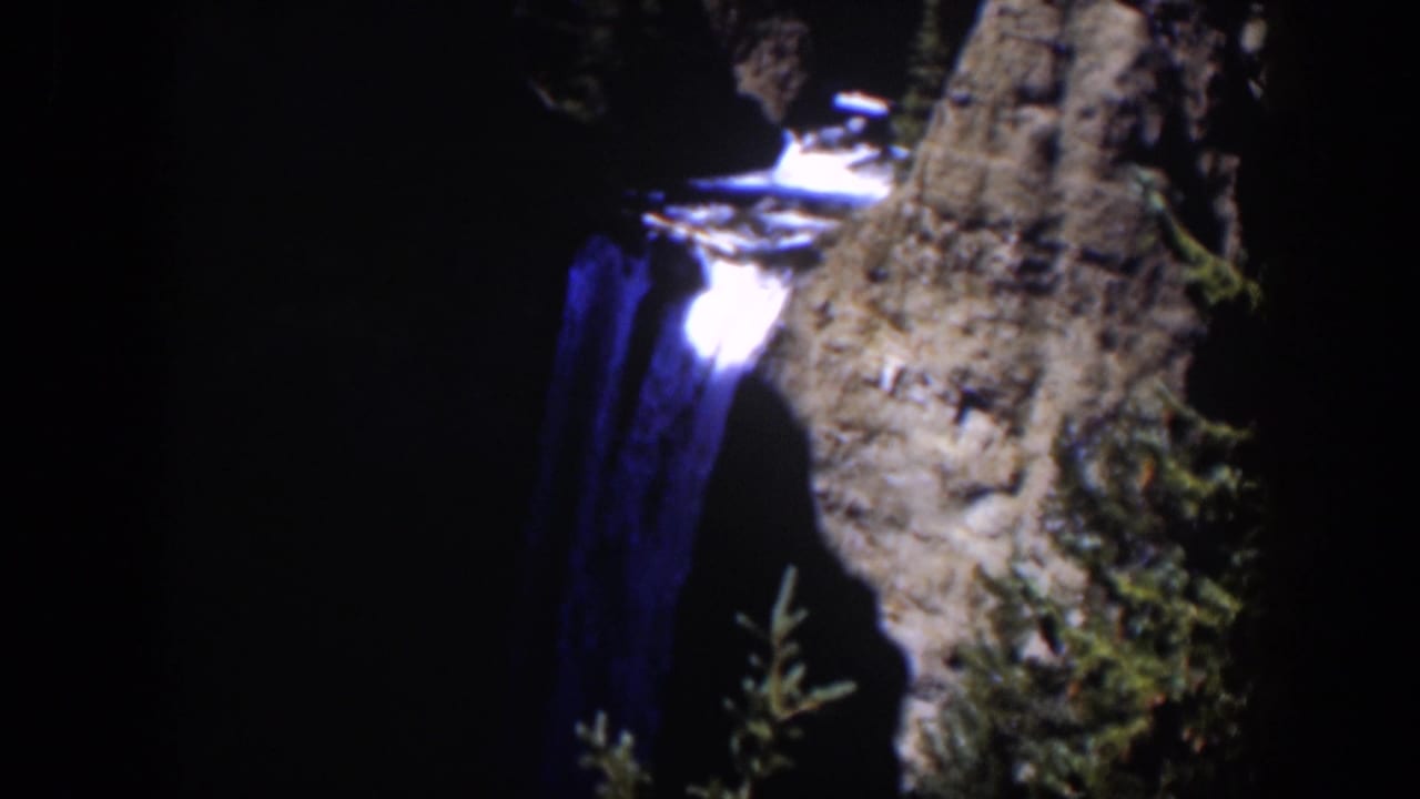 1951 Wyoming 8mm frame of a blue-toned cascade flowing beside a rugged gray cliff, with the scene mostly in deep shade.