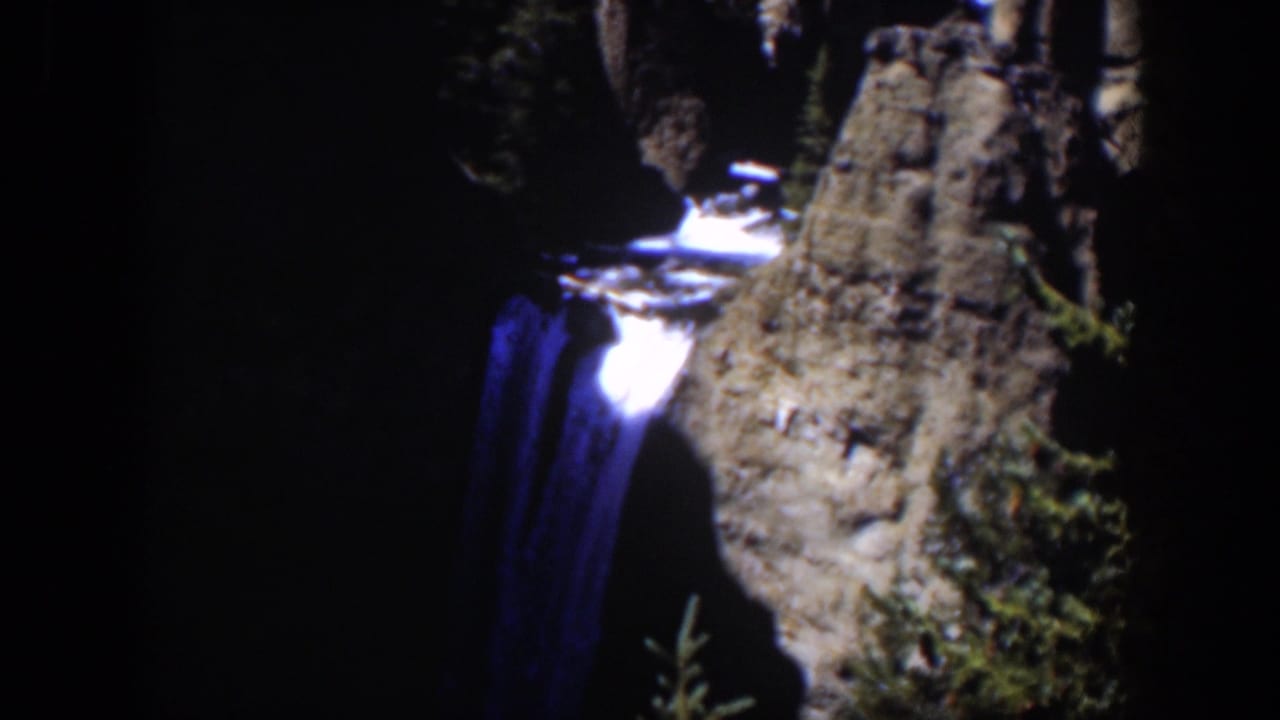 1951 Wyoming 8mm frame showing white water spilling over a rocky edge and down a dark cliff, with conifer branches in the foreground.