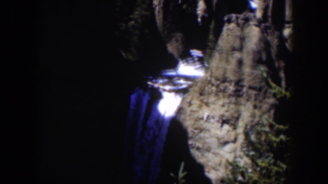 1951 Wyoming 8mm frame showing a waterfall in heavy shadow beside a gray, textured cliff with small patches of vegetation.