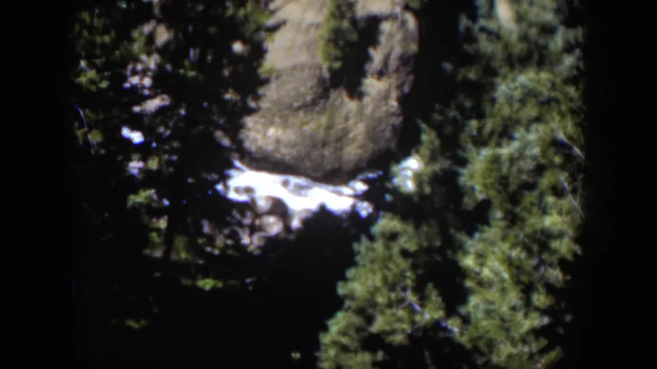 1951 Wyoming home-movie frame showing bright water, rugged rocks, and dense green trees in a mountain setting.